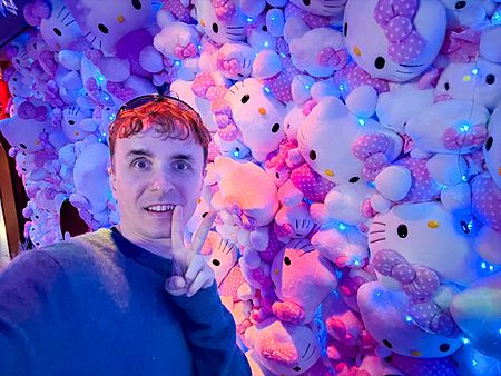 Marco Togni sorride davanti a una parete ricoperta di peluche di Hello Kitty illuminati da luci blu a Hello Kitty Smile.
