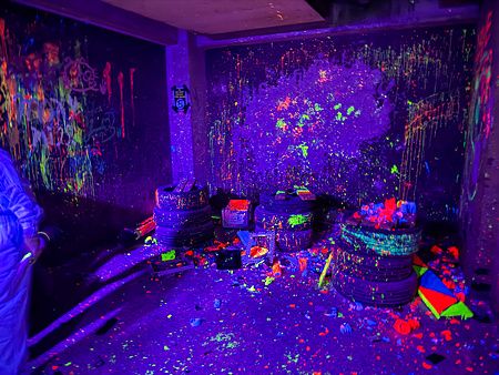 Interno della rage room a Reeast Room a Ikebukuro con pareti e pavimento ricoperti di schizzi di vernice fluorescente.