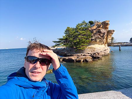 Marco Togni con occhiali da sole e giacca blu si scatta un selfie davanti all'isola di Eshima (Awaji) in Giappone.