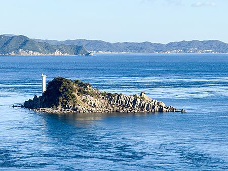 Un'isola vicina al Ponte a Vortice di Naruto con un faro bianco che emerge dalle acque del mare nello stretto di Naruto.