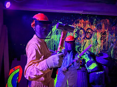 Due persone con tute e caschi protettivi impugnano attrezzi da distruzione nella rage room a Reeast Room a Ikebukuro.