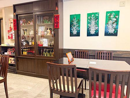 Interno del ristorante Sairaien a Ueno con tavoli in legno, sedie coordinate, una vetrina per bottiglie e quadri verdi.