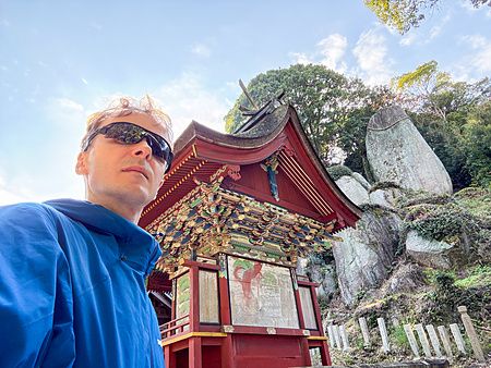 Un uomo in primo piano davanti alla struttura principale del Santuario Iwagami (Isola di Awaji, Giappone) e il masso sacro.