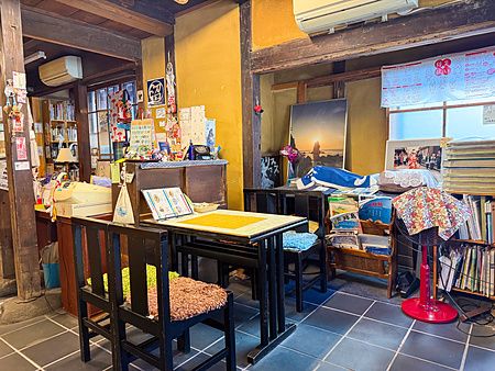 Interno del Yoshijin Battari Cafe sull'isola di Nushima con tavoli in legno, pareti ocra e vari oggetti decorativi.