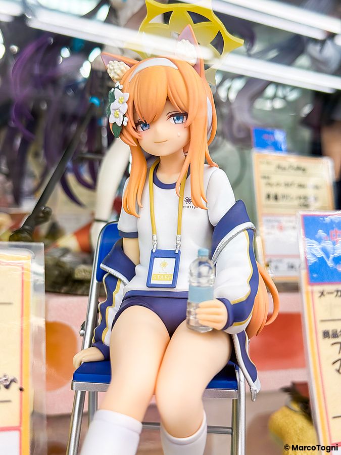 Una figure di un personaggio anime in divisa da staff esposta su una sedia blu presso amiami Akihabara Figure Tower.