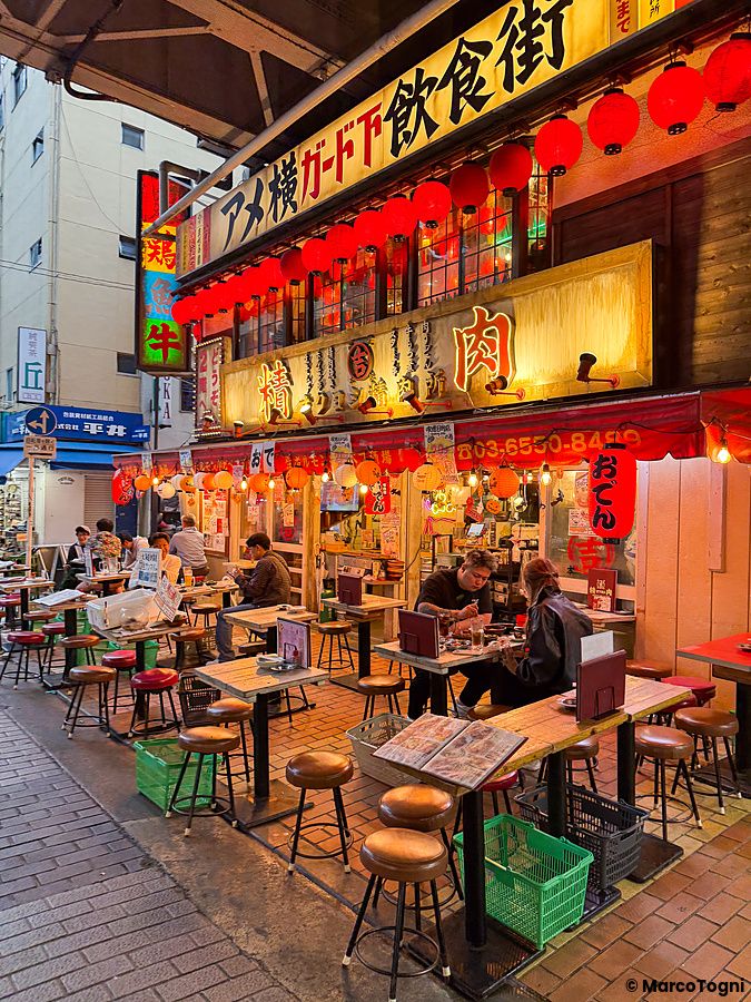 Tavoli all'aperto e persone sedute davanti a un ristorante illuminato da lanterne rosse nella strada Ameyoko a Ueno.