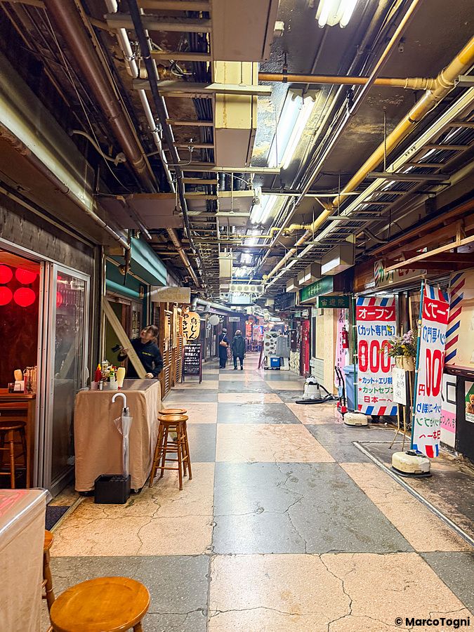 Veduta interna della Asakusa Underground Street con negozi retrò, tubature a vista e persone che camminano nel corridoio.