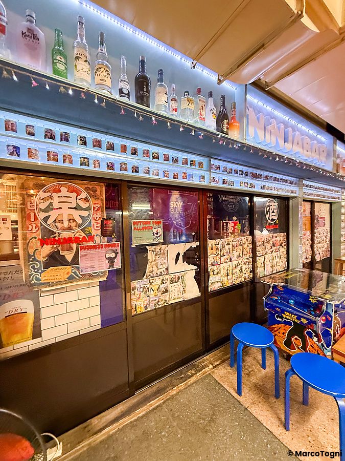Facciata del Ninja Bar nella Asakusa Underground Street con bottiglie, poster e due sgabelli blu davanti all'ingresso.