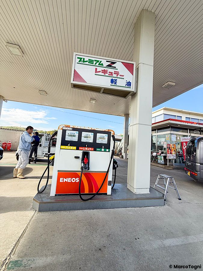 Una stazione di servizio Eneos con pompa di benzina, un uomo, un individuo e un'auto in un piazzale in Giappone.