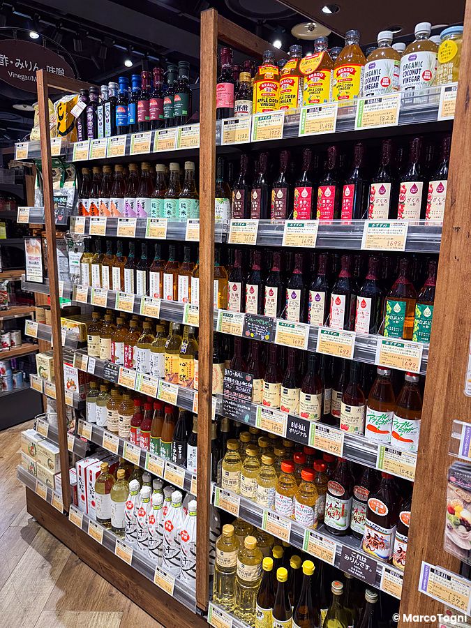 Scaffali in legno di un supermercato Bio-ral in Giappone, ricchi di bottiglie di aceti e condimenti biologici.