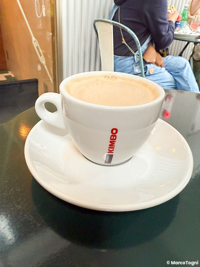 Un cappuccino in una tazza bianca con logo Kimbo su un tavolo scuro presso il ristorante Tutu a Meguro, Tokyo.