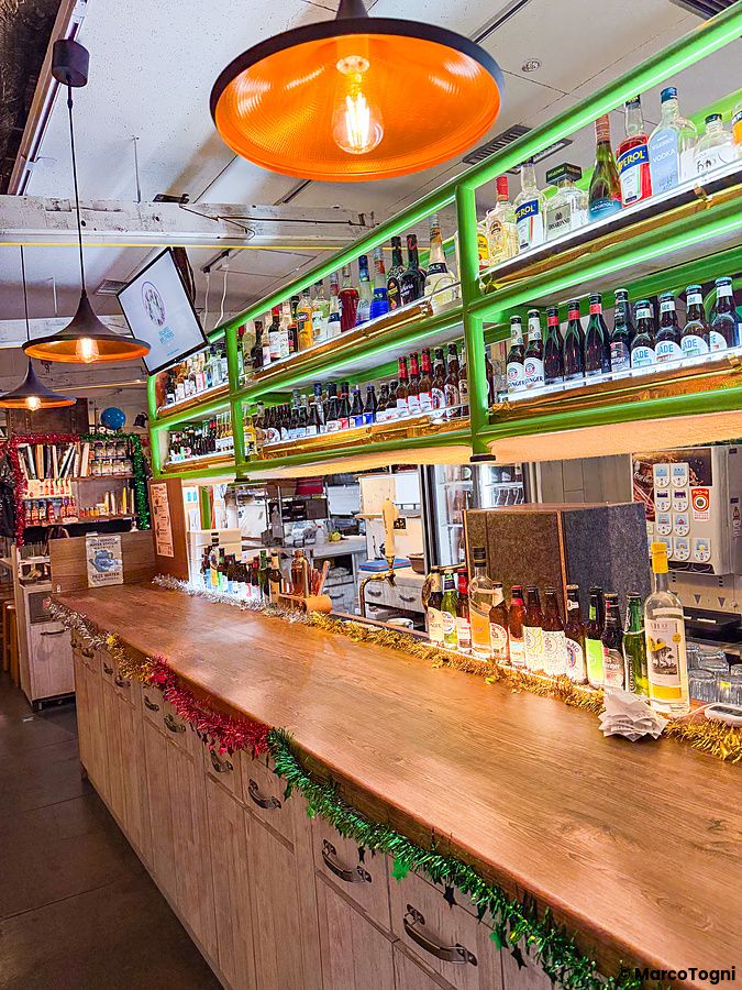 Il bancone in legno di un ristorante Falafel Brothers in Giappone con scaffali verdi pieni di bottiglie e luci calde.