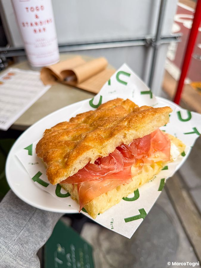 Focaccia con prosciutto su un piattino brandizzato tenuta in mano nel ristorante Tutu a Meguro, Tokyo.