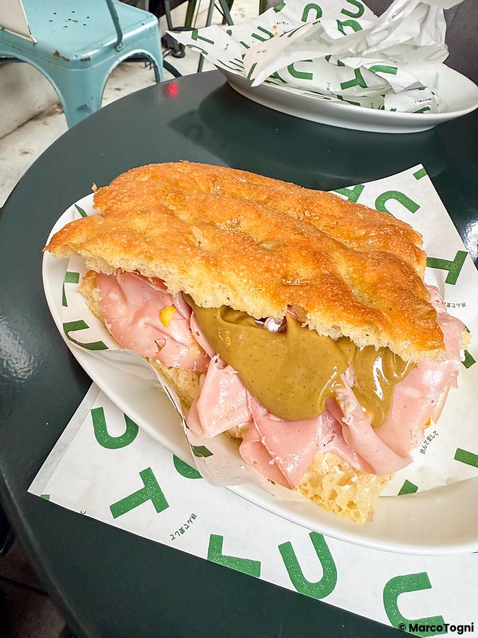 Focaccia con mortadella, crema al pistacchio e ricotta servita su un piatto bianco con carta alimentare marchiata Tutu.