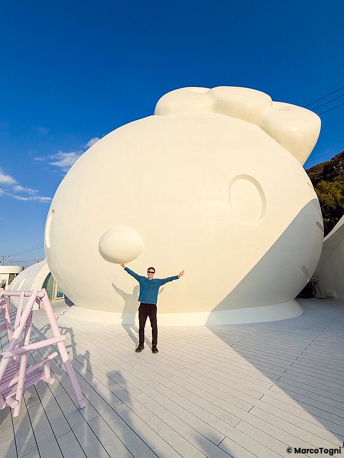 Un uomo è in piedi sul tetto di Hello Kitty Smile davanti alla faccia di Hello Kitty gigante.