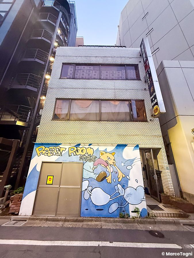 Veduta dell'esterno a Reeast Room a Ikebukuro con un murales colorato sulla facciata dell'edificio a mattonelle.