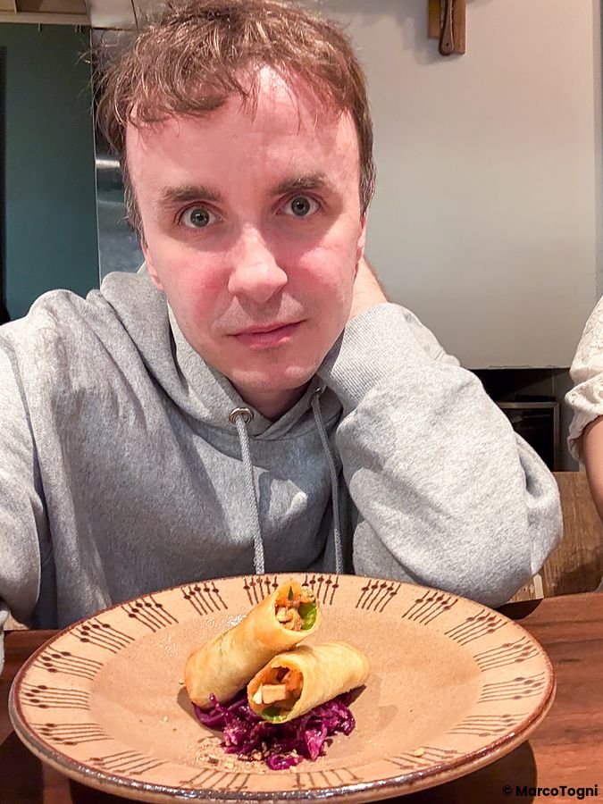 Marco Togni siede a un tavolo del ristorante Mushroom Tokyo davanti a un involtino primavera con funghi e avocado.