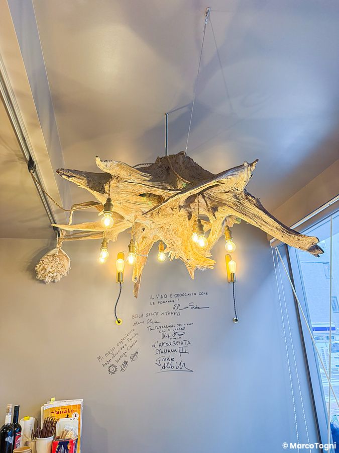 Dettaglio dell'interno a Tutu, ristorante di focacce a Meguro, con un lampadario fatto di radici e scritte sulla parete.