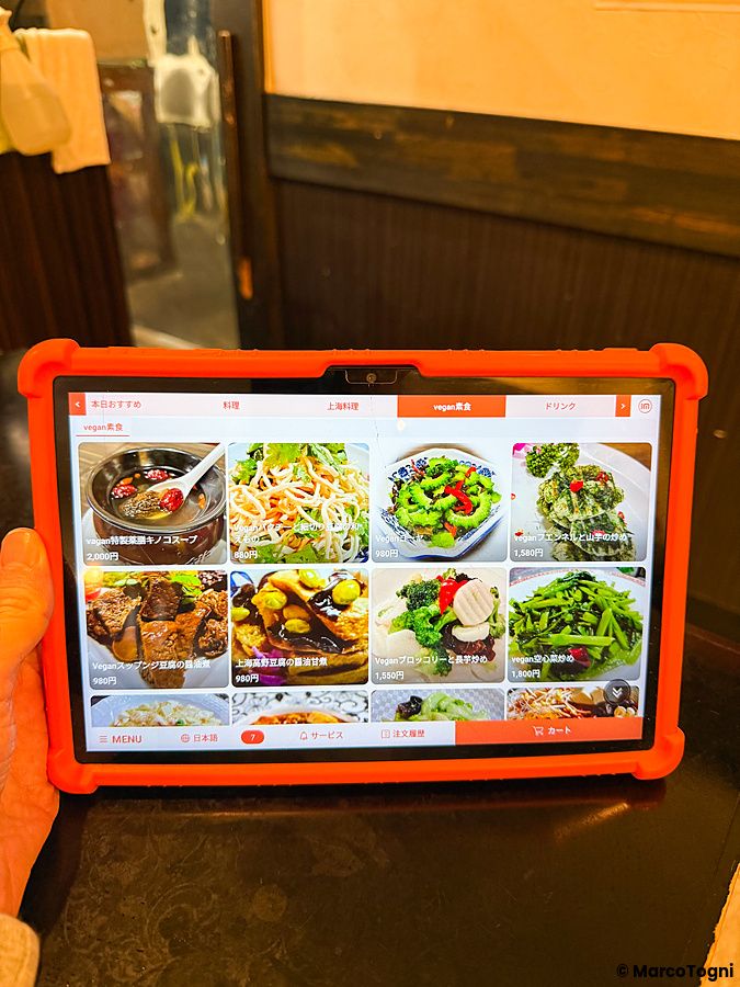 Un tablet con cover arancione mostra il menù digitale con piatti vegani presso il ristorante Sairaien a Ueno.