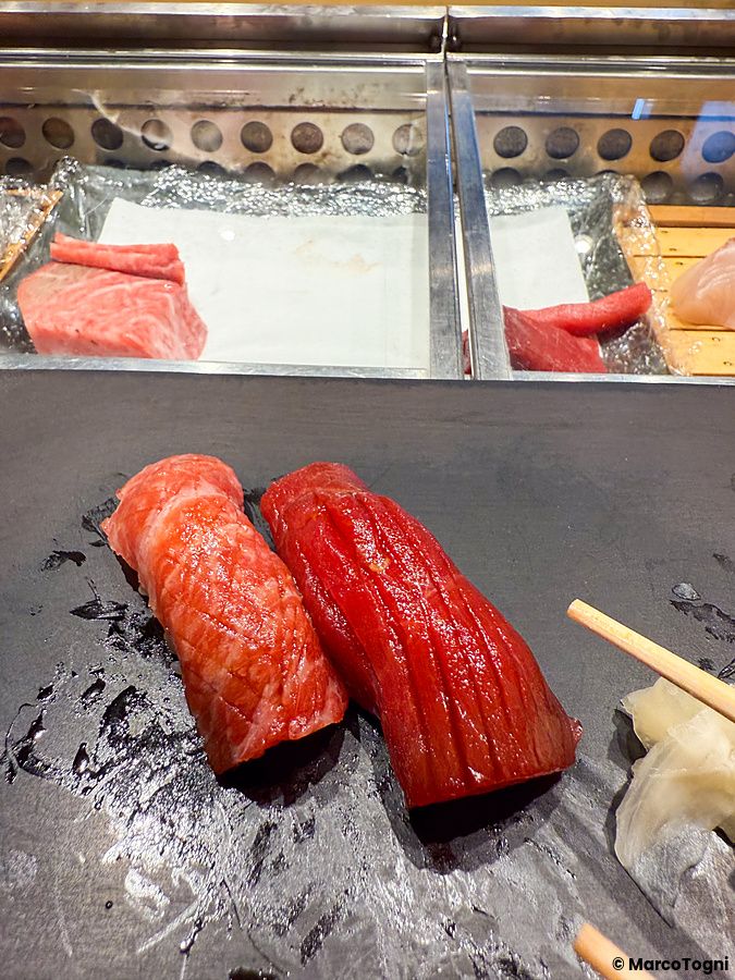 Due nigiri di tonno su un piatto di pietra nera al Sushi & Bar Fujiro Marunouchi Tokyo, con bancone in sfondo.