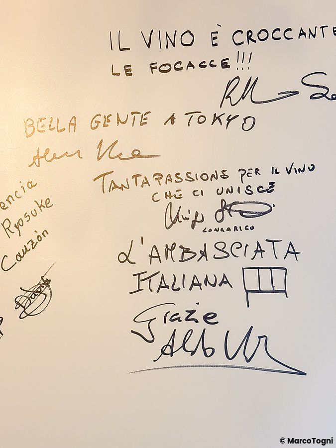 Una parete bianca del ristorante Tutu a Meguro con numerose scritte e firme a mano di visitatori.