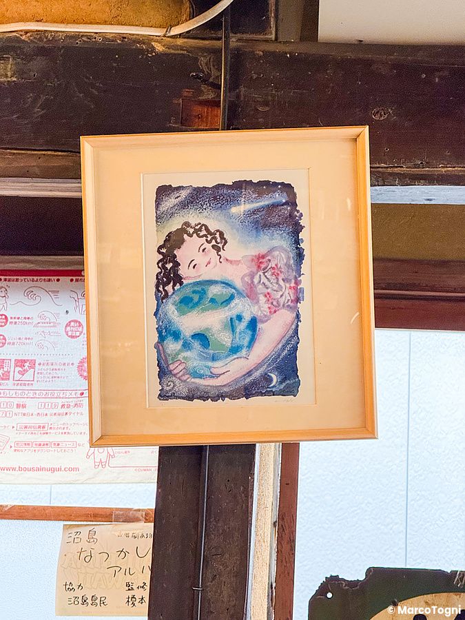 Un quadro incorniciato con una figura femminile che abbraccia il mondo, appeso presso il Yoshijin Battari Cafe.