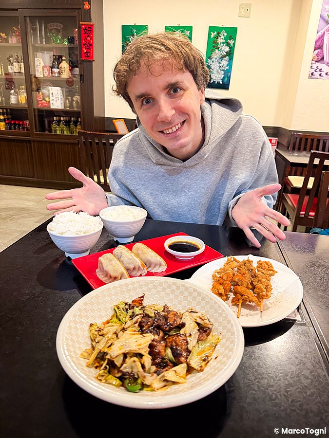Marco Togni sorride al tavolo del ristorante Sairaien a Ueno davanti a verdure saltate con carne di soia, spiedini e gyoza.