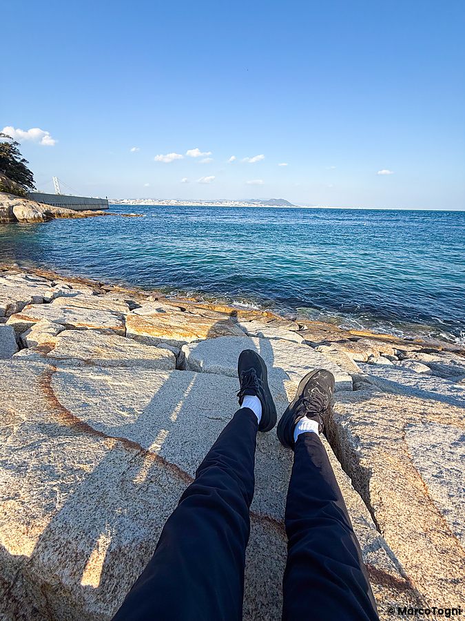 Vista in prima persona delle gambe di una persona seduta sulle rocce di arenaria vicino all'isola di Eshima (Awaji).