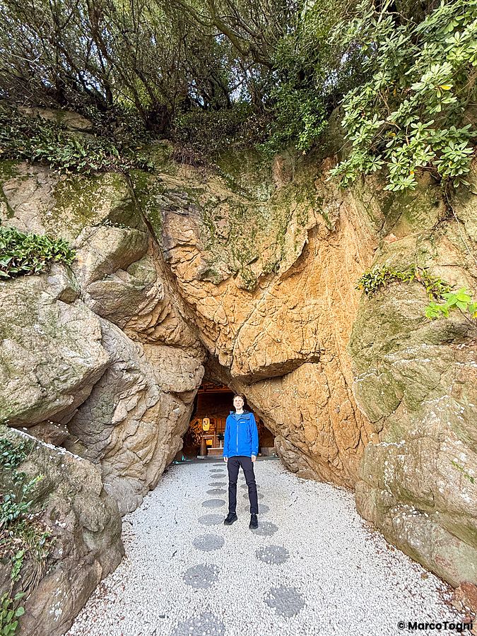 Un uomo in piedi davanti all'ingresso del Santuario Aiga Iwato Shinryu situato all'interno di una grotta marina.