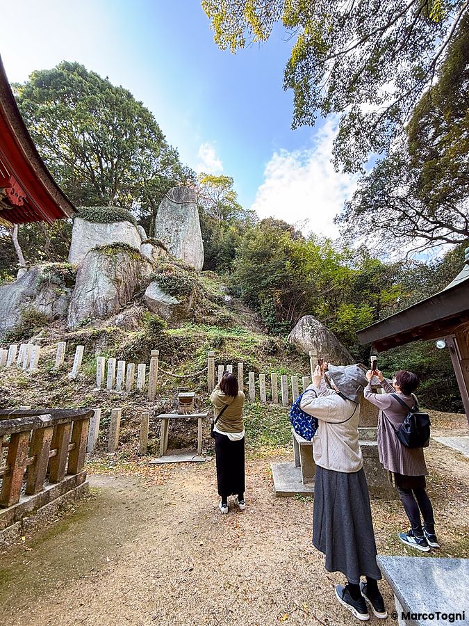 Tre persone fotografano il grande masso sacro all'interno del Santuario Iwagami sull'isola di Awaji, in Giappone.