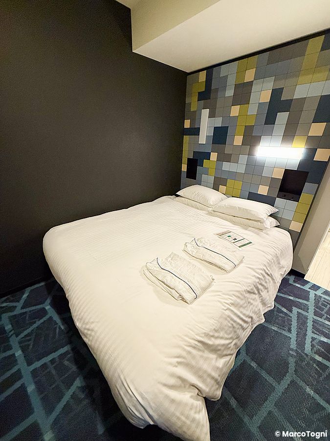 Stanza a JR East Hotel Mets Premier Akihabara con letto matrimoniale, biancheria bianca e testiera a mosaico geometrico.