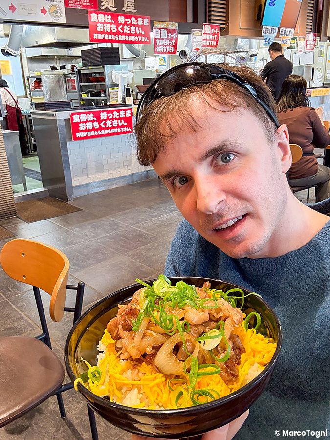 Marco Togni con ciotola di gyudon in stazione di servizio giapponese.