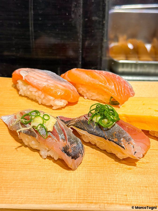 Sushi di salmone e aji su un tagliere di legno.
