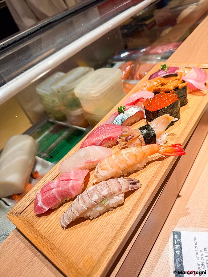 Una fila di nigiri sushi freschi su un vassoio di legno rettangolare presso il ristorante Sushimaru a Shinjuku.