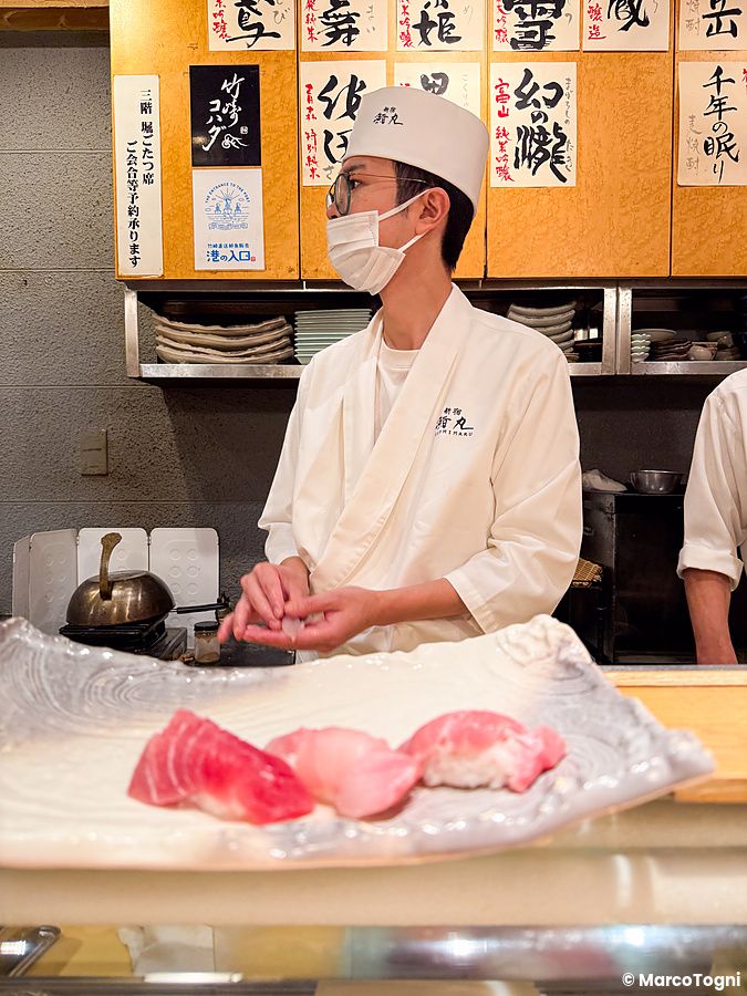 Uno chef di Sushimaru a Shinjuku prepara nigiri di tonno dietro il bancone di legno indossando una divisa bianca.