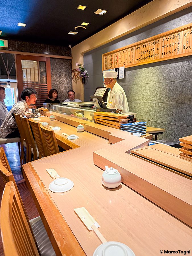 Interno del ristorante Sushimaru a Shinjuku con il lungo bancone in legno e persone sedute davanti allo chef.