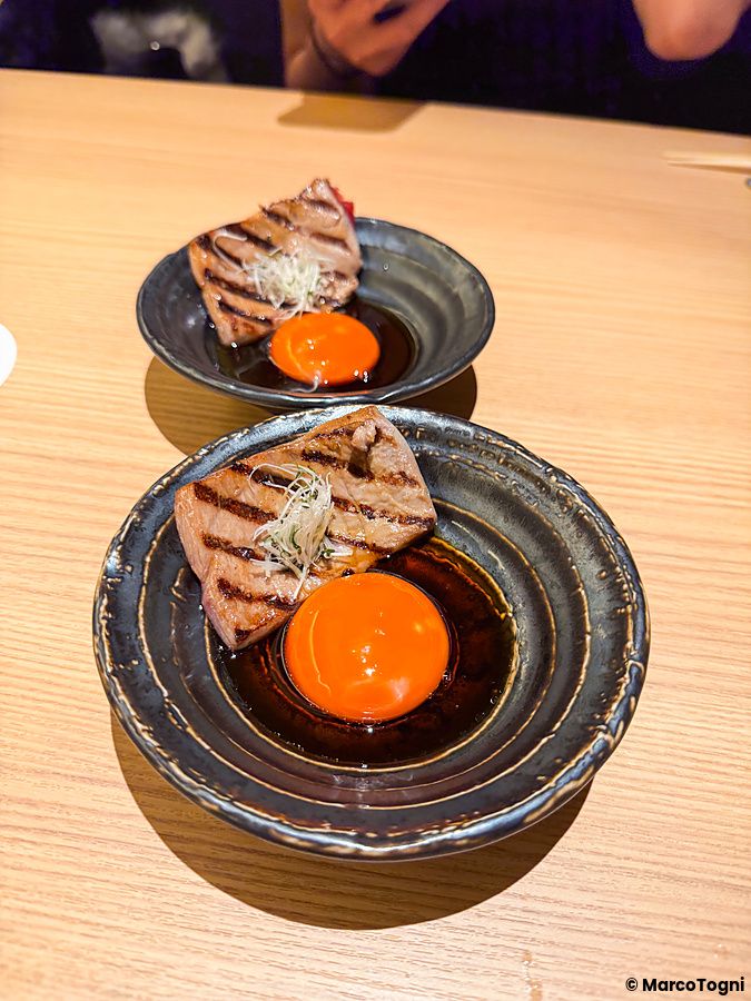 Due piatti con tonno grigliato con uovo, in stile sukiyaki a Yakiuo Ishikawa, serviti su un tavolo di legno.