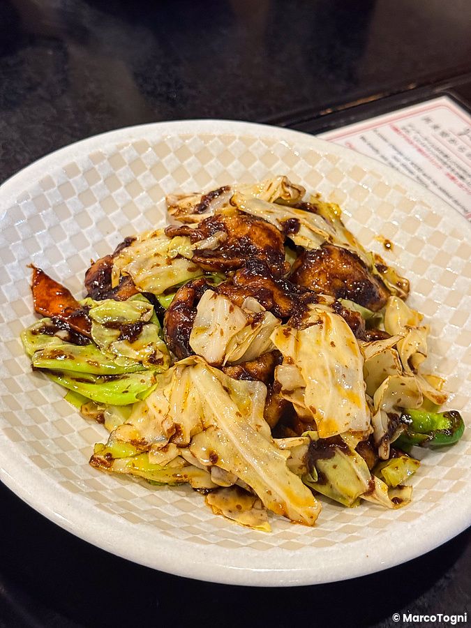 Un piatto di cavolo saltato con salsa scura servito in una ciotola chiara presso il ristorante Sairaien a Ueno.