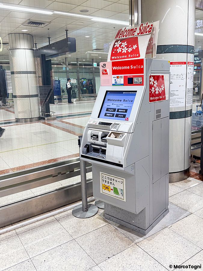 Un distributore di carta Welcome Suica situato all'interno dell'aeroporto di Narita con un individuo sullo sfondo.