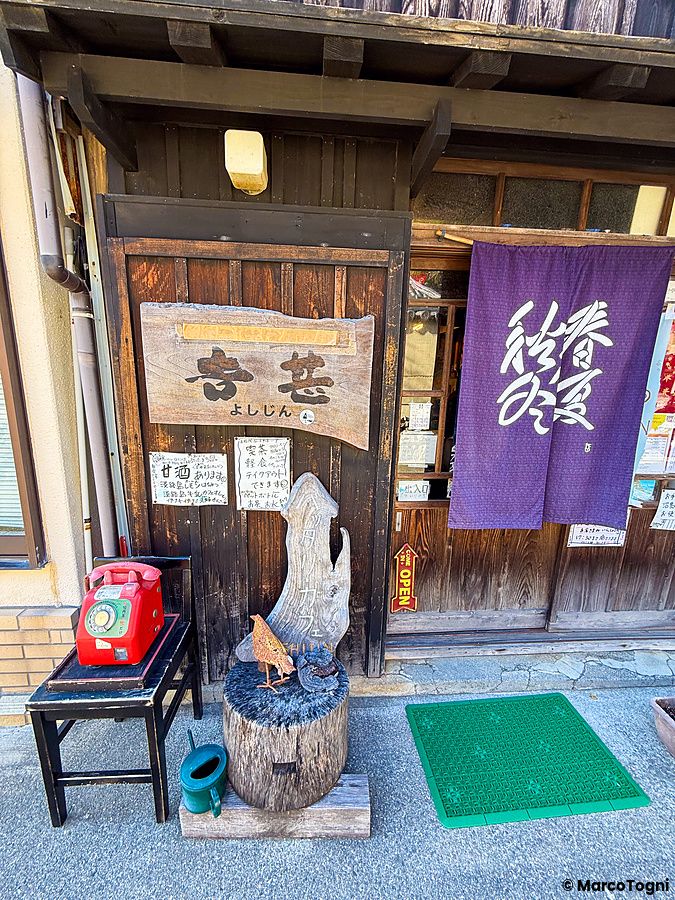 L'ingresso dello storico Yoshijin Battari Cafe sull'isola di Nushima con una tenda noren viola e un telefono rosso.