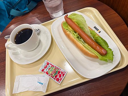 Un caffè e un hot dog con foglia di insalata serviti su un vassoio presso una caffetteria Doutor.