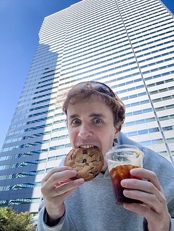 Marco Togni con biscotto del 7 Eleven e caffè davanti a un grattacielo.