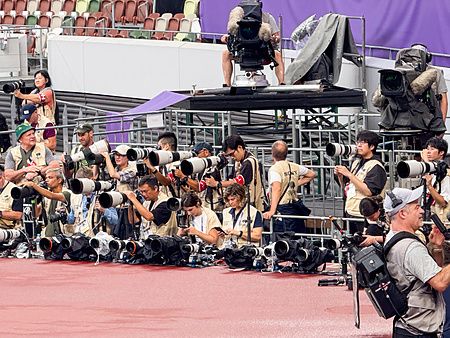Un gruppo di persone con teleobiettivi posizionate lungo la pista all'interno dello Stadio Nazionale Giapponese a Tokyo.