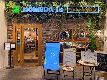 L'ingresso del ristorante vegano Komeda Is a Ginza, con una parete in mattoni, piante verdi e cartelli informativi.