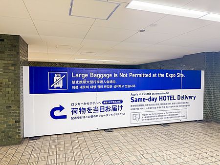 Pannello informativo blu e bianco per deposito bagagli in stazione in Giappone con indicazioni sul servizio di consegna.