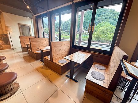 Interno della caffetteria Takao Coffee con tavoli in legno disposti lungo le finestre che danno sul Monte Takao.