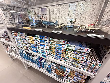 Scaffali pieni di scatole di modellini Tamiya sotto una vetrina con aerei assemblati al Tamiya PlaModel Factory a Tokyo.