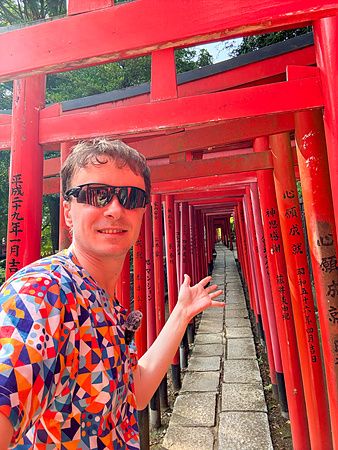 Marco Togni con occhiali da sole davanti a torii rossi del santuario Nezu, Tokyo.