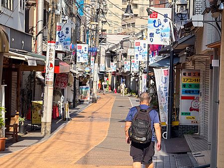 Una persona con zaino cammina lungo la via principale di Yanaka Ginza tra negozi e insegne tradizionali giapponesi.
