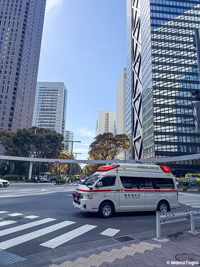 Un'ambulanza del Tokyo Fire Department transita in un incrocio circondato da alti edifici in vetro a Shinjuku.